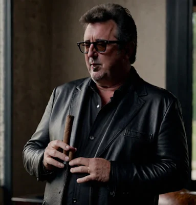 Vince Gill wearing sunglasses hiding a cigar wearing leather blazer