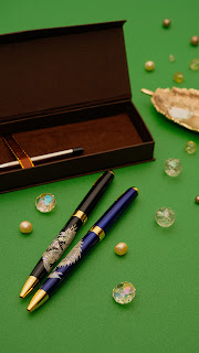 Elegant mother-of-pearl inlaid pens with gold accents on a green background, accompanied by a pen box and decorative items.