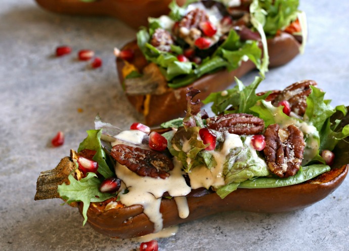 Recipe for salad served inside a roasted honeynut squash and topped with pomegranate arils, candied pecans and a tahini dressing.