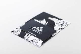 Na obrazku jest karta podarunkowa sklepu Adidas. Jest ona koloru czarnego w białe wzory i ma biały napis oraz logo Adidasa.