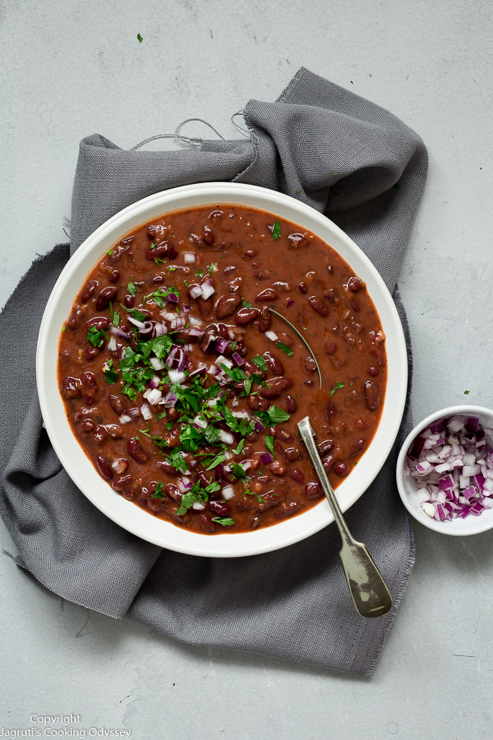 Afghan style red kidney bean curry served in a white bowl and garnished with fresh green coriander and chopped red onion