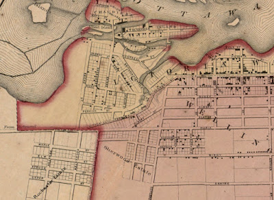 Crop of a map from 1863 which shows Ottawa with limits at Bank Street (East), Centre Street (now Somerset, South), City Limits (Now City Centre Ave, West), and the Ottawa River (North), with city boundaries and wards indicated by colouring. Wellington Street and its extensions George St and Victoria Terrace, have a dotted line indicating the boundary between Victoria Ward (north of the line) and Wellington Ward (south of the line). The streets and individual lots (where blocks have been subdivided) are shown, and black squares indicating the location of buildings are on about a third of them. Between Bay and Concession Line (now Bronson), Wellington Street makes an abrupt turn southwest and is labelled George St which heads to the east approach to Pooley's Bridge (which is neither drawn nor marked) and continues to Hill Street (not labelled, now Brickhill) after which it becomes Victoria Terrace where it meets Richmond Road at a shallow angle on the southern boundary of LeBreton Flats. Richmond Road is drawn as continuous in line with Maria Street (now Richmond). North of the extension of Maria Street (Laurier), nothing is drawn west of Broad Street inside or outside city limits, aside from a label 