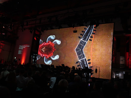 Photo of a graph display take at SFSoundBox. Horizontally symmetric pattern based on a Renaissance painting. Elements include a lute's fretboard and a feathered hat, on a red background.