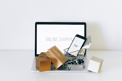 Brown and white paper bags around a smartphone in a silver shopping cart in front of a computer at a check out desk.