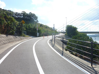 Towards the top of the Shimanami Kaido bikeway leading up to the Tatara Bridge on Ikuchijima. There's a sign warning about wild pigs (animals) and the Tatara bridge cables are visible 