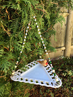 This hanging dish bird feeder features a triangle shaped white glass plate with scalloped edges. 