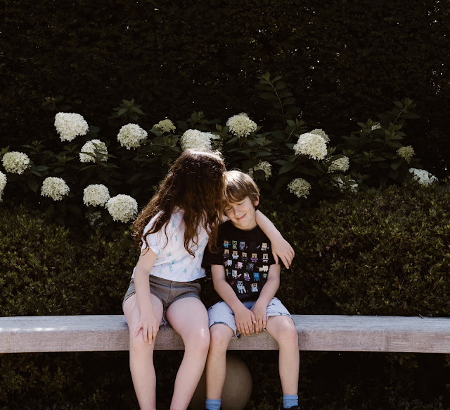 Sister hugging her brother while sitting in garden bench