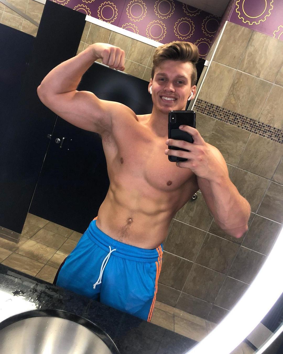 cute-fit-bare-chest-guy-smiling-bathroom-mirror-selfie-biceps-flex