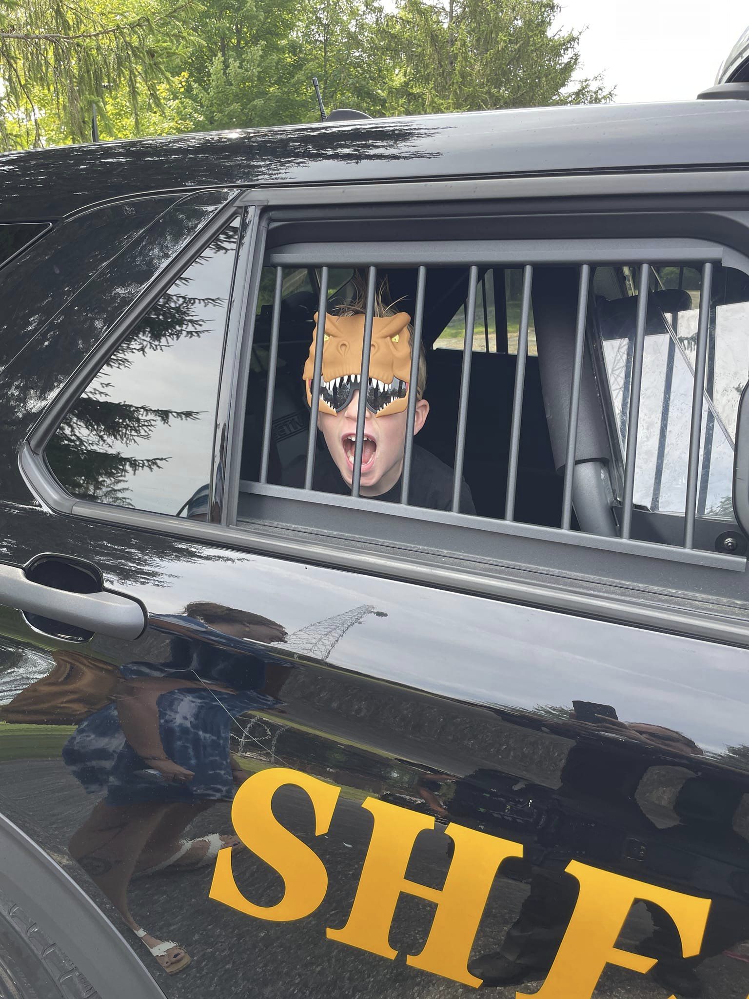 boy with mask on in back of sheriff car