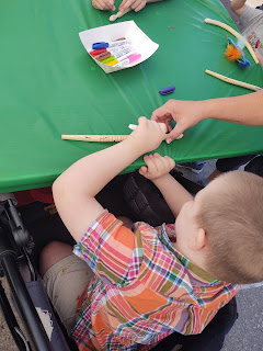 a boy in an orange plaid shirt draws on a wooden toy snake at Art Splash 2022, as seen from above