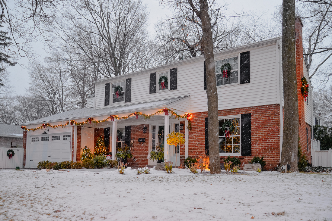christmas wreaths on windows of colonial house with white fence with garlands and red bows