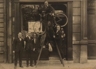 Opening of the Max Ernst exhibition at the gallery Au Sans Pareil, May 2, 1921. From left to right: René Hilsum, Benjamin Péret, Serge Charchoune, Philippe Soupault on top of the ladder with a bicycle under his arm, Jacques Rigaut (upside down), André Breton and Simone Kahn. Par Auteur inconnu — http://www.dadart.com/dadaism/dada/024-dada-paris.html, Domaine public, https://commons.wikimedia.org/w/index.php?curid=31878747