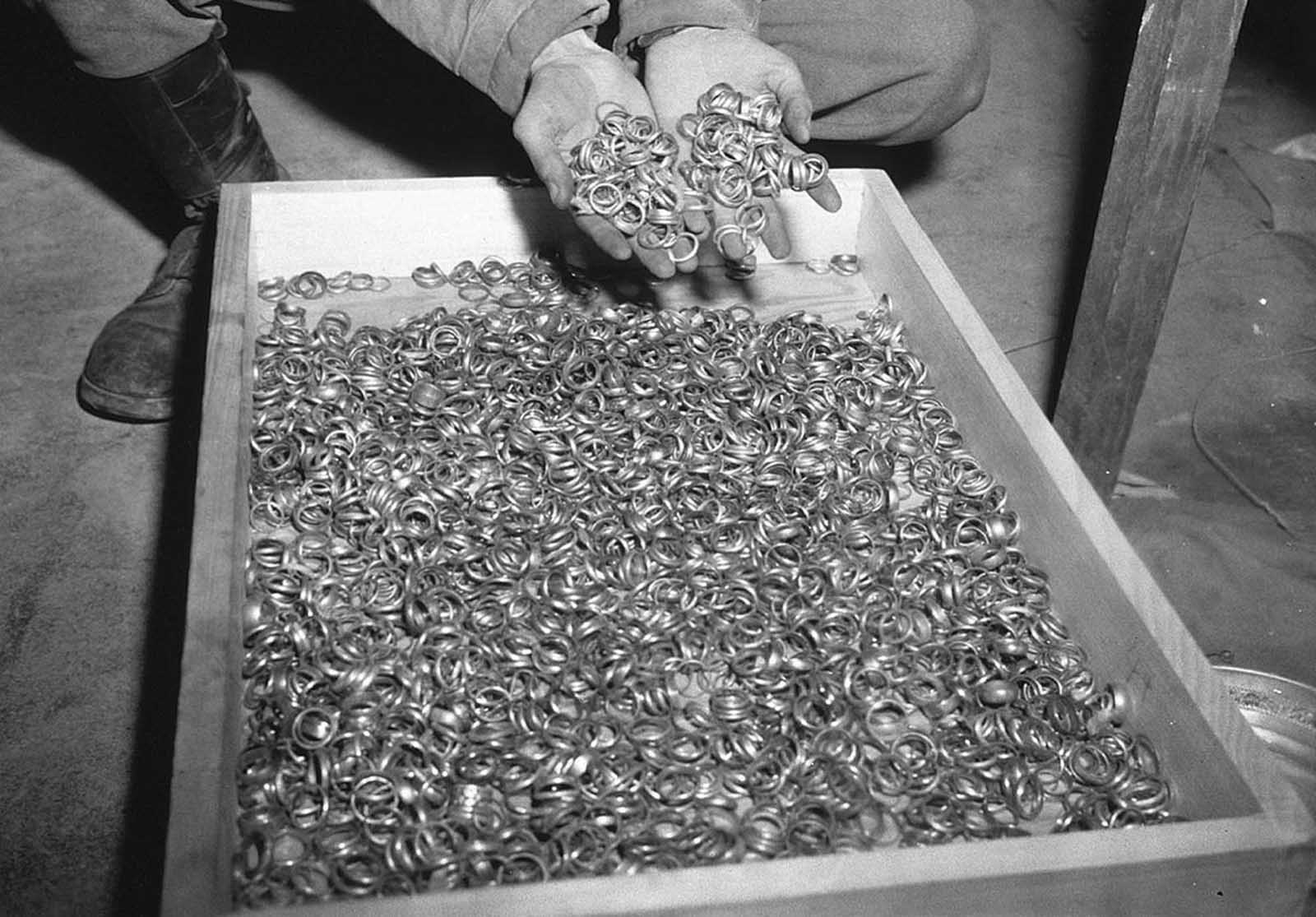 A U.S. soldier inspects thousands of gold wedding bands taken from Jews by the Germans and stashed in the Heilbronn Salt Mines, on May 3, 1945 in Germany. 