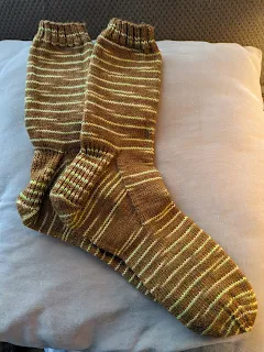 A pair of handknit wool socks. They are brown with mini stripes of green