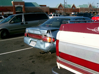 A blue car with its backend bashed in strapped together with clear tape that is usually used for shipping packages