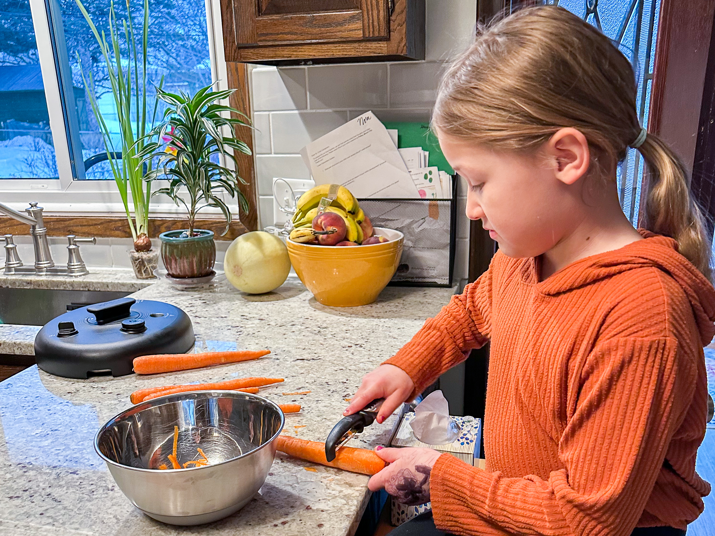 Elementary child peels carrots at kitchen counter in Montessori home