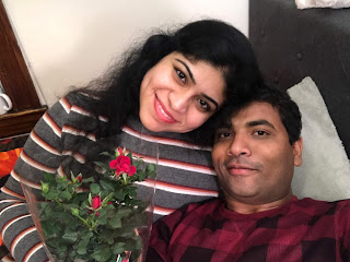 A photograph of a couple with a red rose plant in their hands