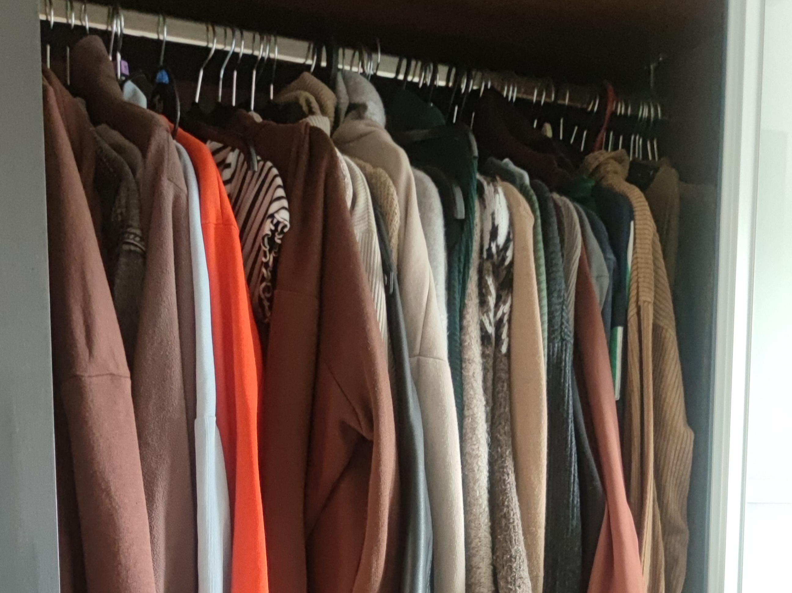 An image of an open wardrobe with a hanging rail full of different items of clothing.