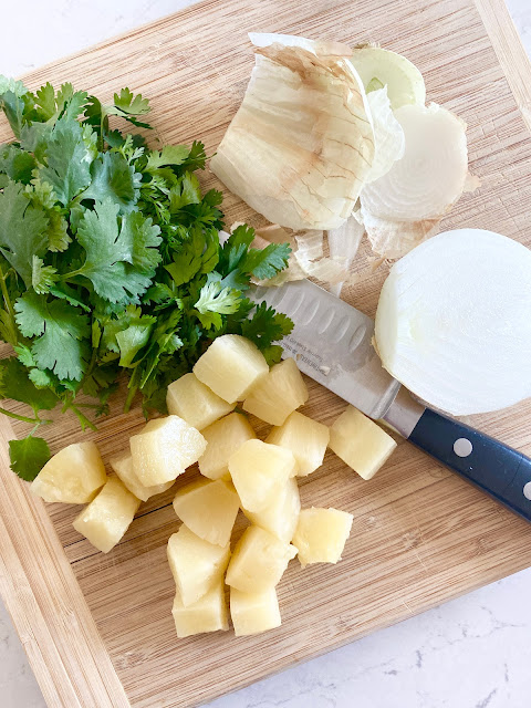 Cilantro, pineapple and onion on a wooden cutting board.