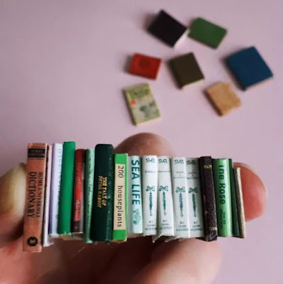 A hand holding a row of one-twelfth scale miniature vintage-style books with some extra scattered in the background