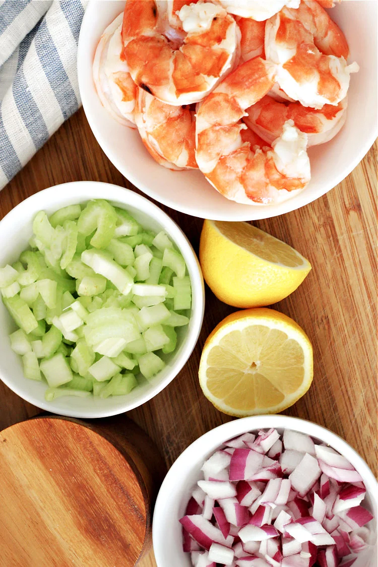 Overhead view of shrimp in a white bowl and other ingredients for cold shrimp salad recipe