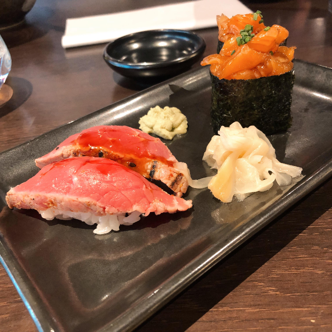 Beef nigir and salmon gunkan sushi on a plate with small piles of pickled ginger and wasabi