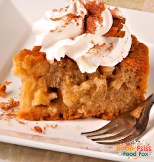 This image shows a slice of cinnamon apple cake on a white plate with a fork. The cake is topped with a dollop of whipped cream and a sprinkle of cinnamon.