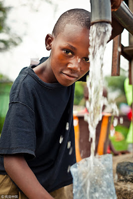 Africa boy is smiling at camera and using water