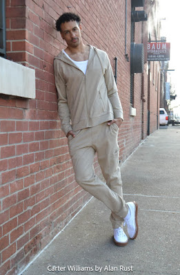 Carter leaning against a brick wall wearing a beige track suit