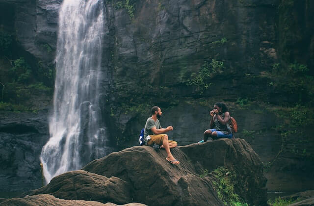 Man and woman by a big waterfalls talking and drinking