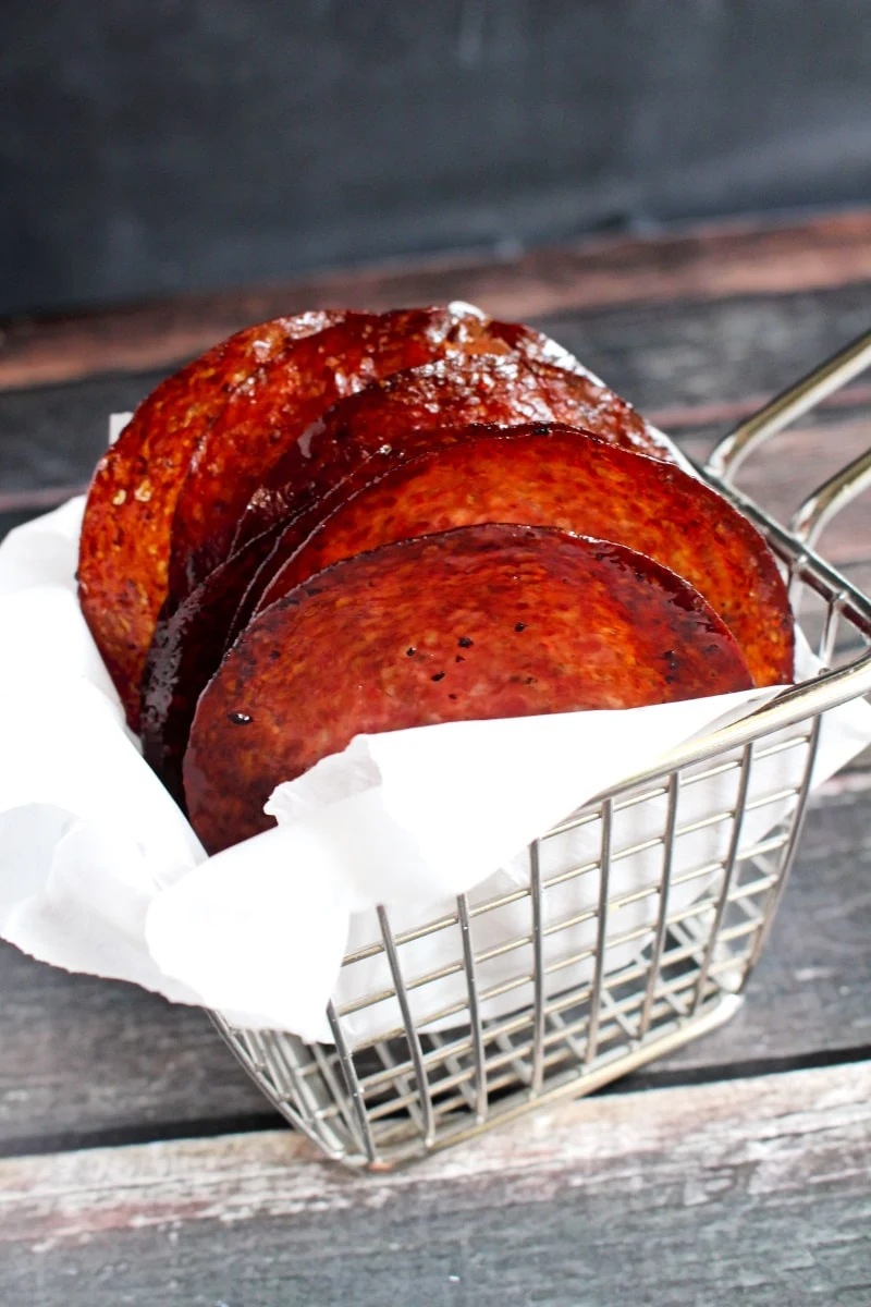 Side view of salami chips in a wire basket with a black background.