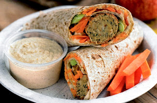 Home-made tortillas wrapped around falafel and mixed vegetables sliced in half and served with chickpea hummus and carrot sticks