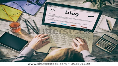 A blogger working from a computer with a mobile phone, pencils, cup of beverage, notepads, a pen on a notepad on top of the work table.