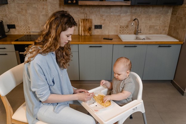 A mom feeds a baby in a highchair.