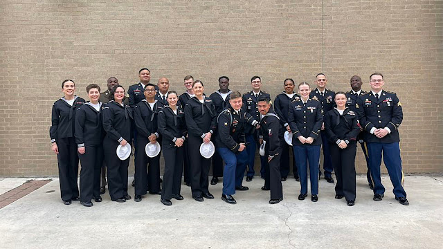 A group of students stand together at graduation against a brick wall