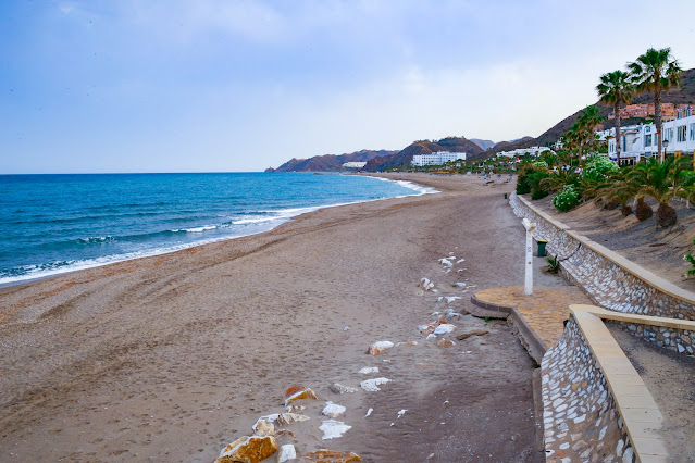 Playa de arena con el paseo marítimo a su espalda y las azules aguas del mar a su frente