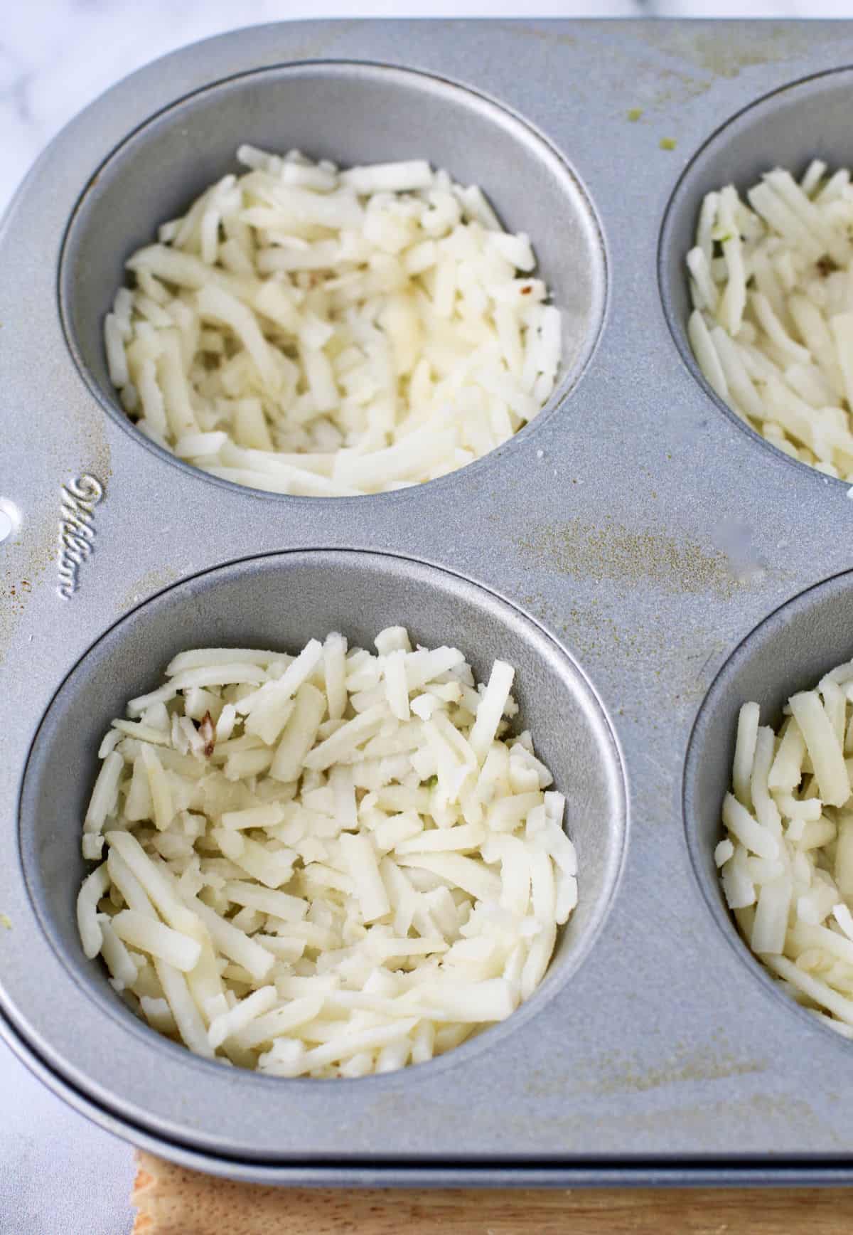 Hash brown potatoes pressed into a muffin tin before baking.