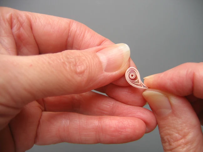 hands pinching a quilled coil into a shaped teardrop