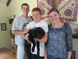 Connor, Austin and Allie, Austin's sister stand in front of the fireplace.  Austin is holding Coach.