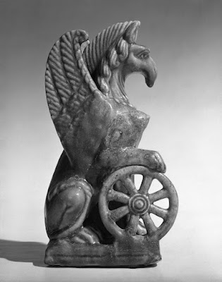 Nemesis in the form of a female griffin, resting on the wheels of fate