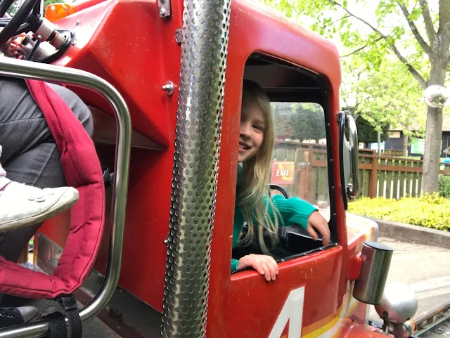 View of the side front window of a red truck with a girl smiling out the window