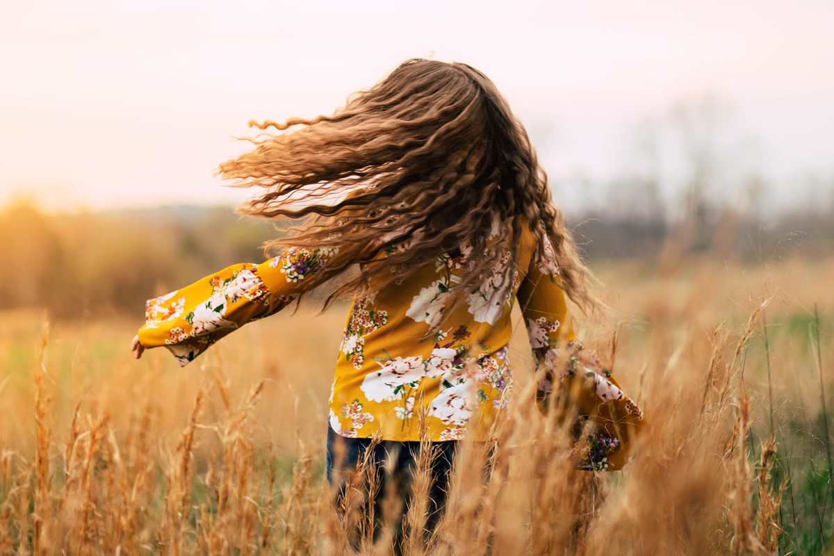 woman with long curly hair is posing in a field