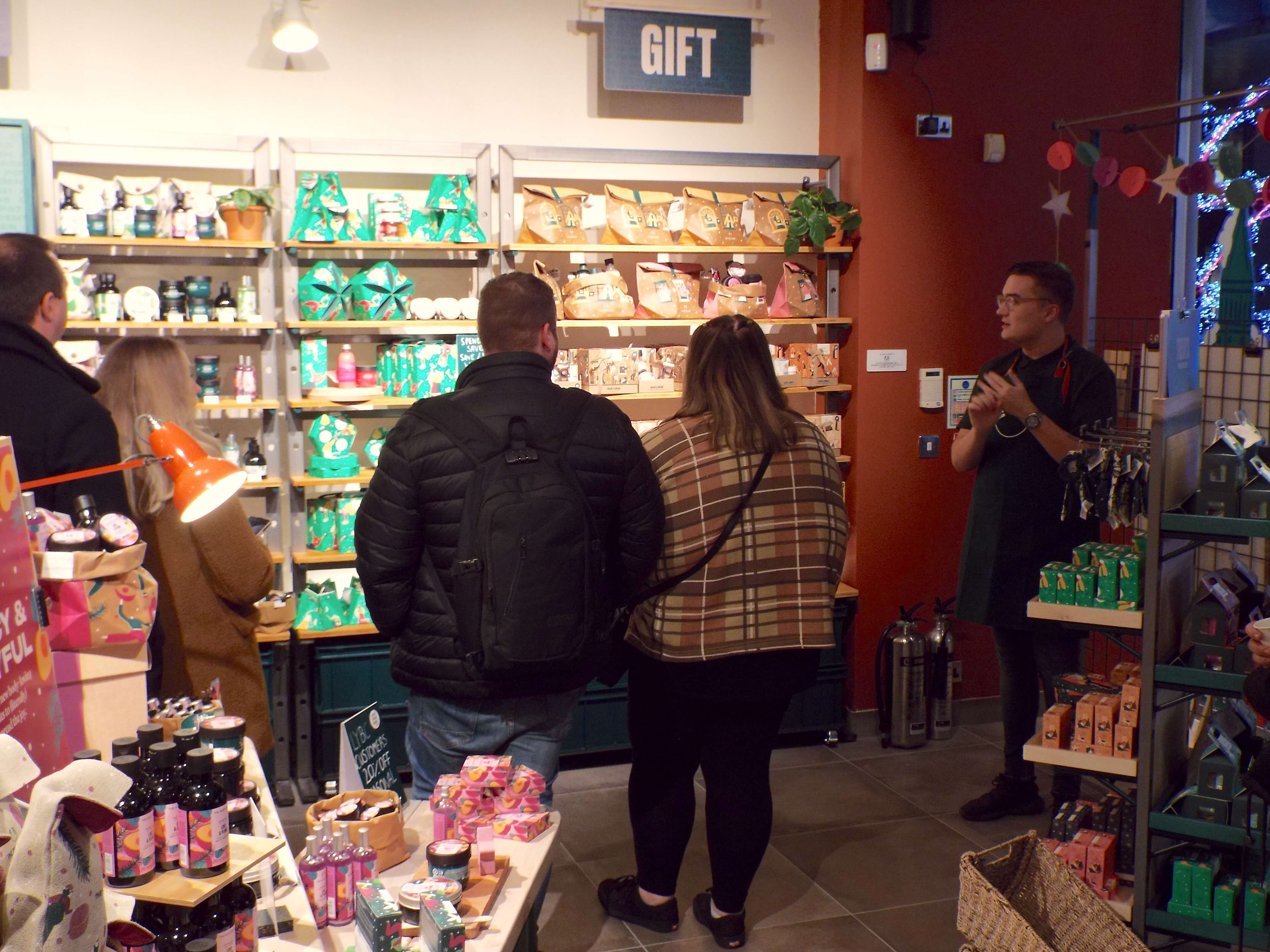 Two couples look at the display of Christmas gifts sets, whilst Ryan beside them talks about the range.