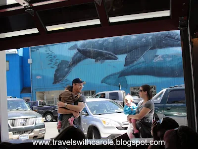 parents bearing children stand in front of Wyland Whaling Wall mural in front of Mo's Original Restaurant in Newport, Oregon