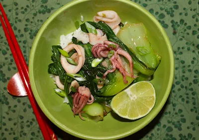 Serving bowl of stir fried squid with baby bok choy over rice.