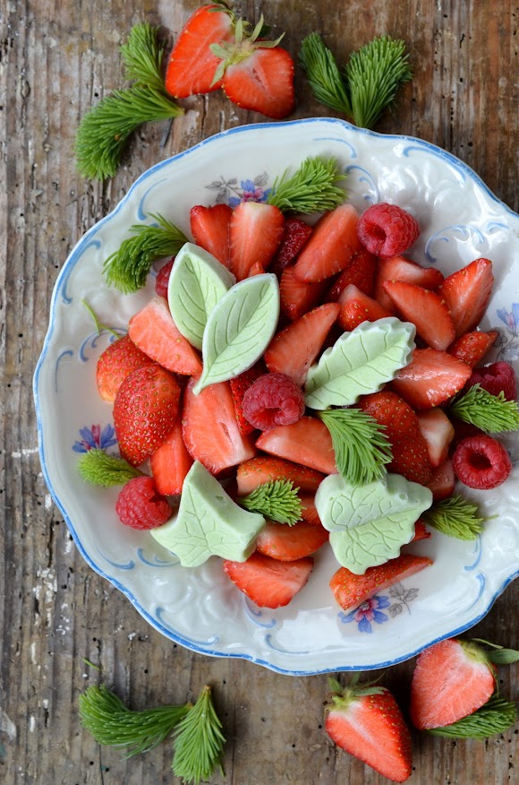 Bild von hellgrünen Eispralinen auf einem frischen Erdbeersalat. Das Dessert liegt auf einem hübschen Teller mit blauem Rand.