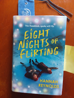 Cover of Eight Nights of Flirting: two teenagers laying in the snow, blue background, title in yellow font