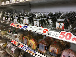 Two shelves of rice-balls, both triangular and round, in a local 7-Eleven