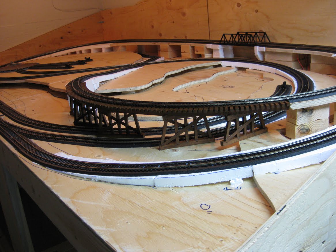 Model railroad benchwork with completed track on foam roadbed and painted wooden train trestle