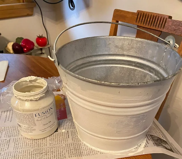 Photo of a thrifted galvanized bucket being painted in Raw Silk.